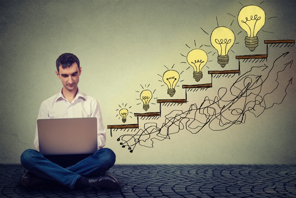 Happy young man entrepreneur working on computer sitting on a floor in his office successful in increasing internet website traffic. Promotion, company growth concept. Isolated on gray wall background-1